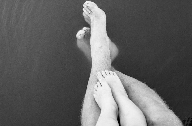 Baby's feet on top of the fathers legs on water.