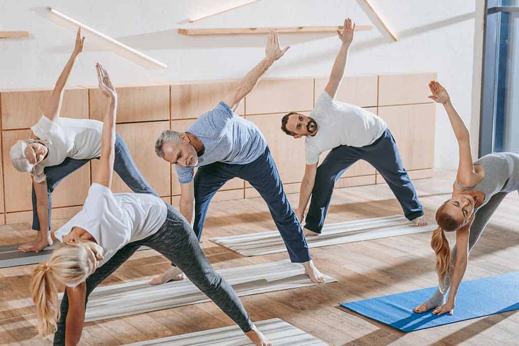 Senior people with instructor exercising on yoga.